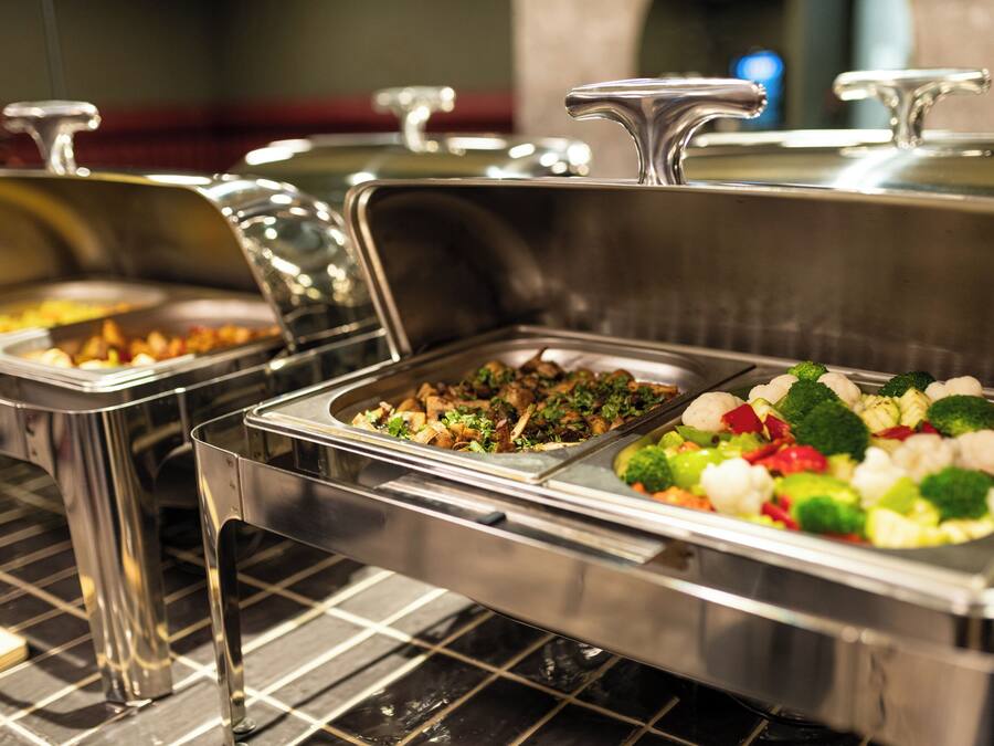 A buffet with various food items, including vegetables and meats, in stainless steel serving containers.