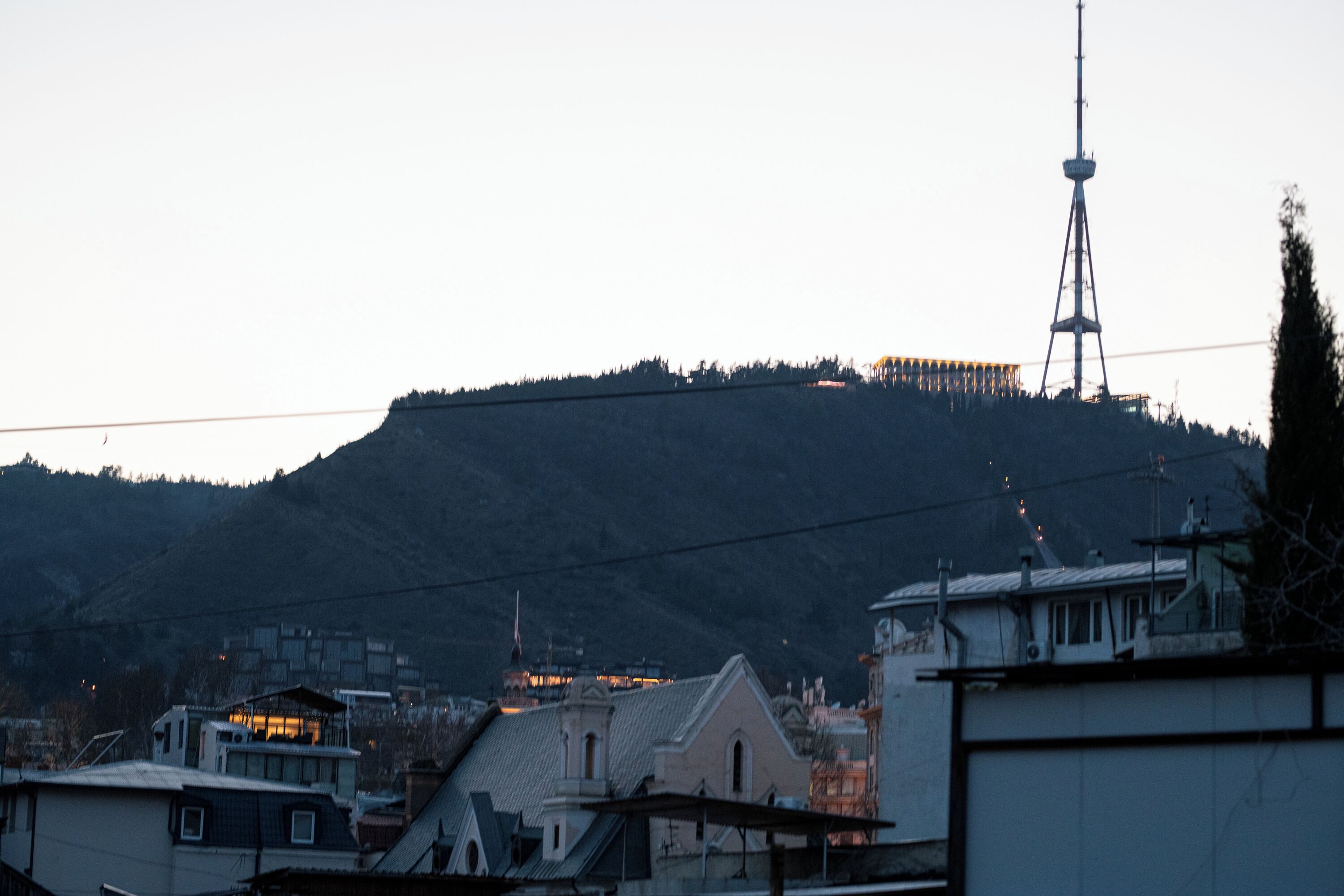 A cityscape with a prominent tower, buildings with flat roofs, and a hilly backdrop.