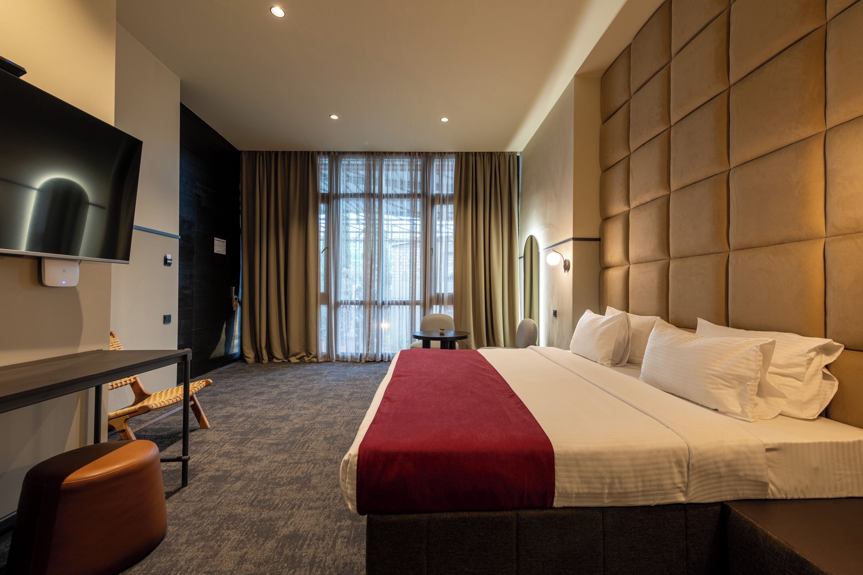 A hotel room with a large bed, a desk, a chair, a television, and a window with curtains.