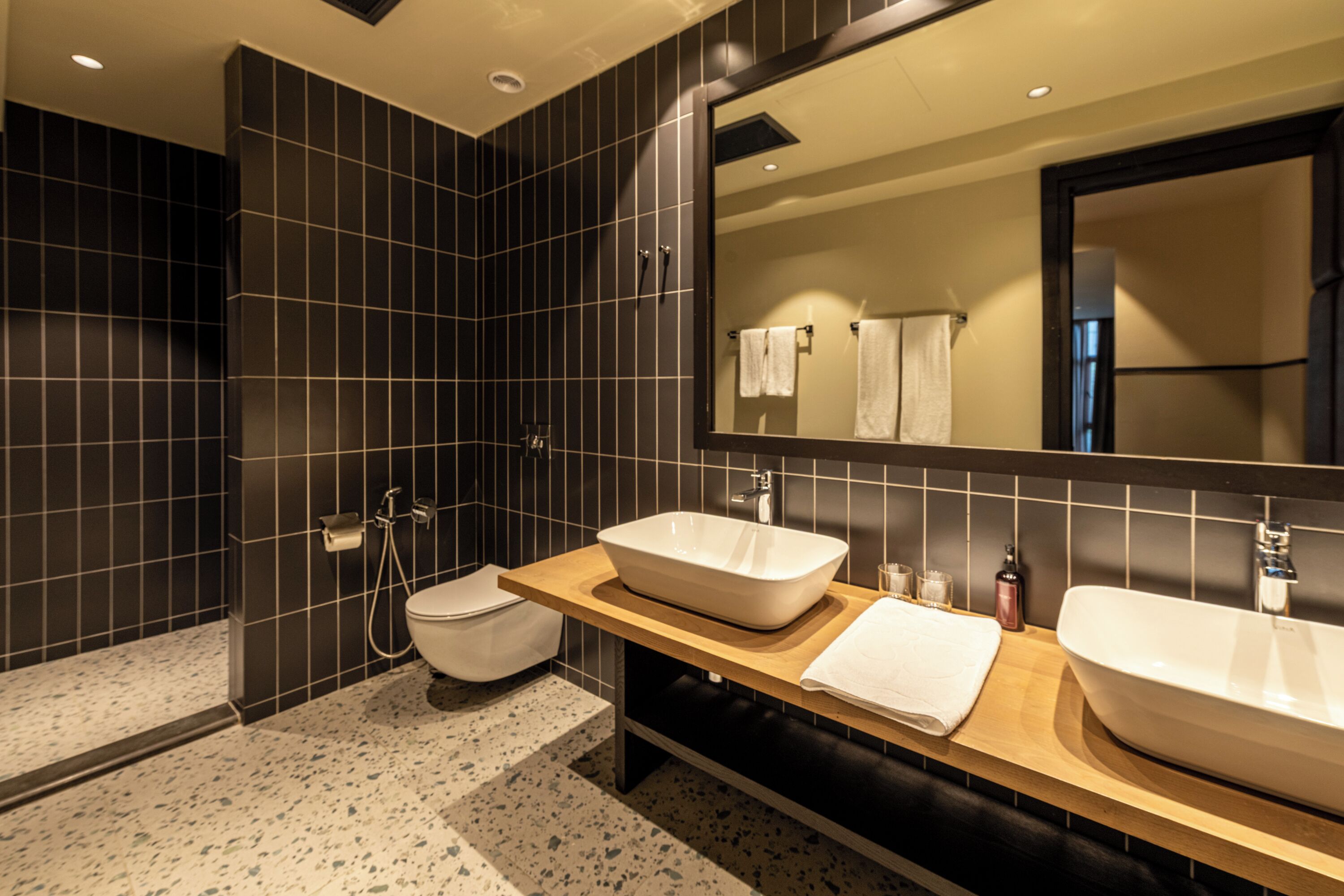 Un baño moderno con un espejo grande, dos lavabos, un inodoro y una ducha.