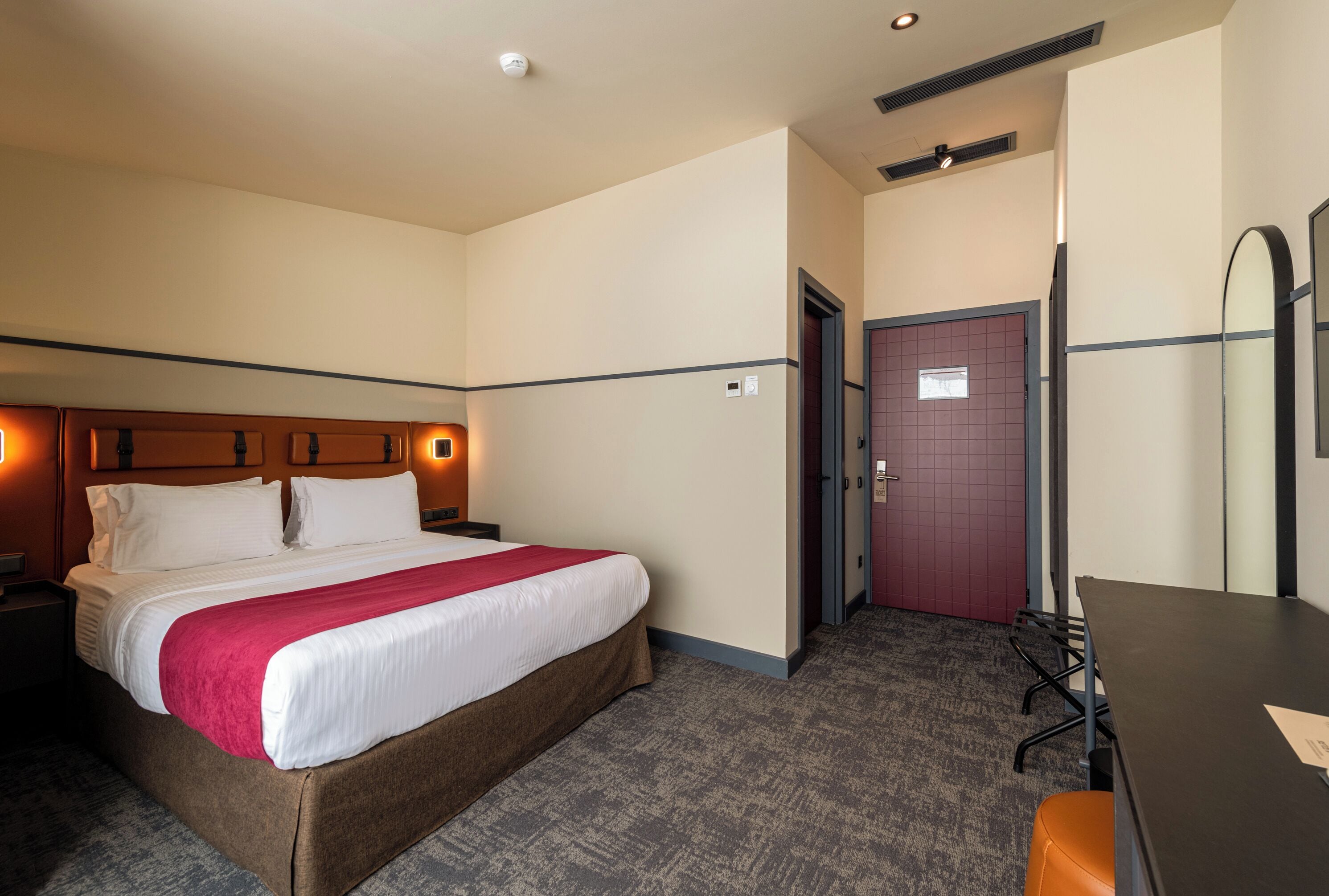 Ein Hotelzimmer mit Bett, Schreibtisch, Stuhl, Tür und Spiegel.