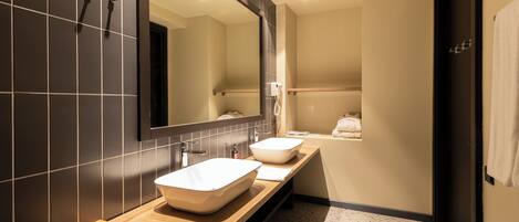 A modern bathroom with a large mirror, two sinks, and a shower area.