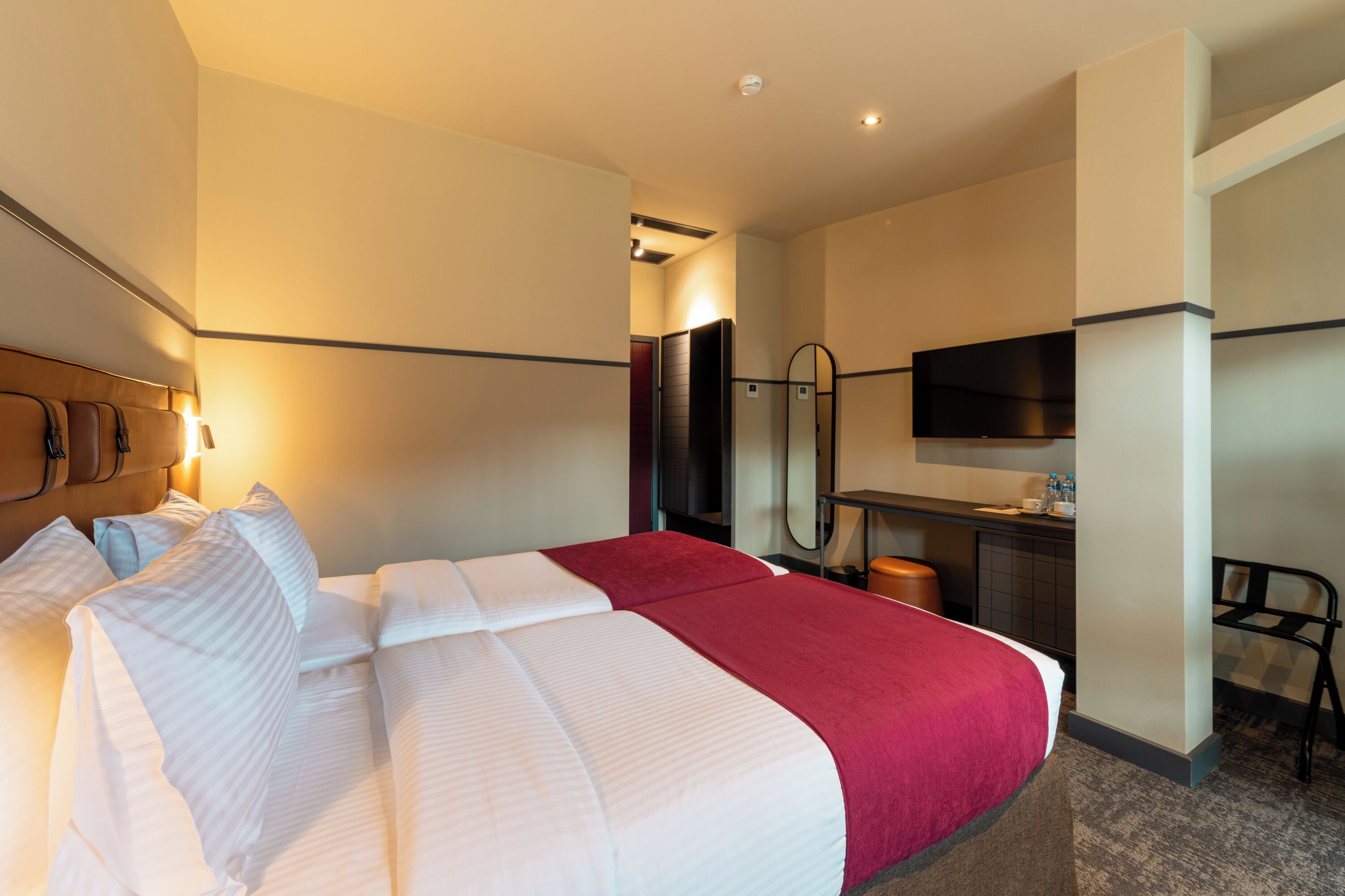 Ein Hotelzimmer mit einem Bett, einem Schreibtisch, einem Sessel, einem Fernseher und einem Spiegel.