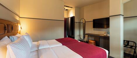 Ein Hotelzimmer mit einem Bett, einem Schreibtisch, einem Sessel, einem Fernseher und einem Spiegel.