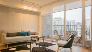 A modern living room with a sofa, a coffee table, a chair, and a large window with a view of buildings. - w Inviting 3BR w Balcony in Hip Miraflores (Lima)