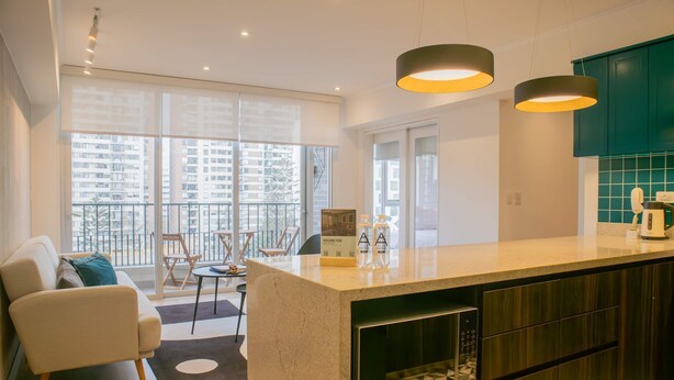 A modern kitchen with a central island, a dining area with a sofa and chairs, and large windows offering a view of the city. - w Inviting 3BR w Balcony in Hip Miraflores (Lima)
