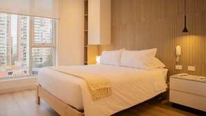A modern hotel room with a large bed, bedside tables, a nightstand, a lamp, and a view of the city through large windows. - w Inviting 3BR w Balcony in Hip Miraflores (Lima)