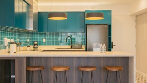 A modern kitchen with teal cabinets, a stainless steel refrigerator, a coffee maker, and a bar stool area. - w Inviting 3BR w Balcony in Hip Miraflores (Lima)