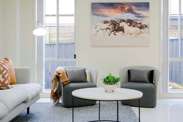 Un salon avec un canapé gris, deux fauteuils, une table basse ronde et un tableau représentant des chevaux accroché au mur.