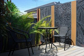 Une terrasse avec deux chaises et une table, entourée d’une clôture décorative ornée d’un motif de feuilles.