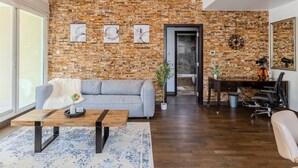 A spacious living room with a brick wall, a grey sofa, a wooden coffee table, and a chandelier. - Luxury 1BR in Dubai Marina Beside Vida Yacht Club (Dubai)