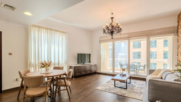 A modern living room with a dining area, a chandelier, a flat-screen TV, and large windows with a city view. - Luxury 1BR in Dubai Marina Beside Vida Yacht Club (Dubai)