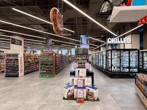 Et dagligvarebutiksmiljø med køleelementer, hylder med snacks og en udstilling af legetøjsbiler.
