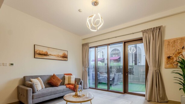 Ein großzügiges Wohnzimmer mit einem grauen Sofa, einem runden Couchtisch und einer großen Schiebeglastür, die auf eine Terrasse im Freien führt.