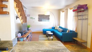 A living room with a blue sofa, a TV, a wooden staircase, and a map on the wall. - Townhome in Crested Butte | 2 Bedroom | Walk to Elk Ave | Parking (Crested Butte)