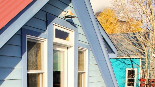 A blue house with white exterior walls and a wooden deck. There are white Adirondack chairs and a small round table on the deck. - Townhome in Crested Butte | 2 Bedroom | Walk to Elk Ave | Parking (Crested Butte)