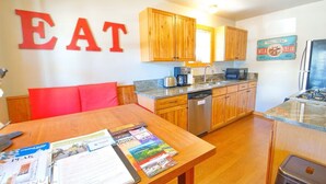 A compact kitchen with wooden cabinets, a dishwasher, and a refrigerator. A table with magazines is in the foreground. - Townhome in Crested Butte | 2 Bedroom | Walk to Elk Ave | Parking (Crested Butte)
