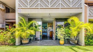Entrada de un edificio con un patio cubierto, plantas en macetas y un conjunto de asientos.
