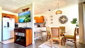 Una cocina moderna con armarios de madera, un refrigerador empotrado, un televisor y un comedor con sillas de madera y una mesa de vidrio.