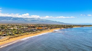 Un pueblo costero con propiedades frente a la playa, un cielo azul despejado y montañas a lo lejos.