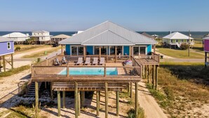 A beachfront house with a pool on a wooden deck, surrounded by other houses.