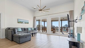 A spacious living room with a sectional sofa, a coffee table, and a flat-screen TV mounted on the wall.