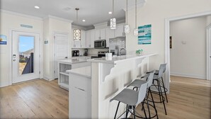 A modern kitchen with white cabinetry, a central island with bar stools, a microwave, and a refrigerator.