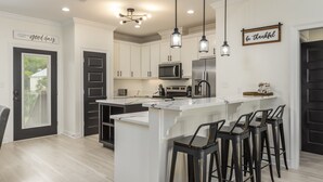 Une cuisine moderne avec des meubles blancs, un îlot central doté de tabourets et des luminaires suspendus.