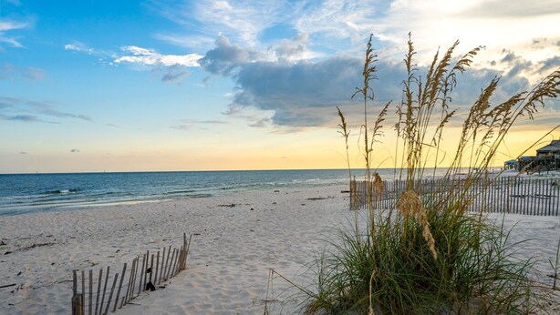 A beach with sand, waves, and a wooden fence.