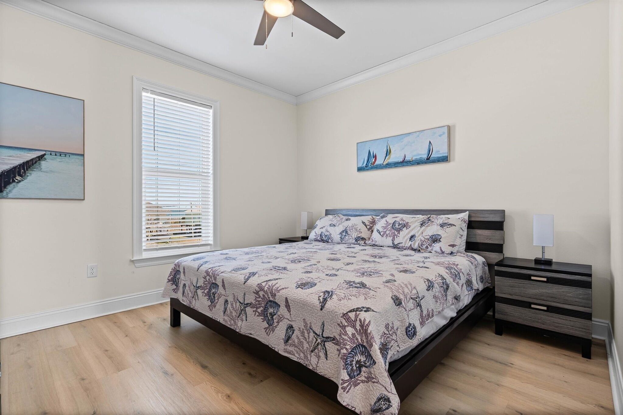 A bedroom with a bed, nightstands, a ceiling fan, and artwork on the walls.