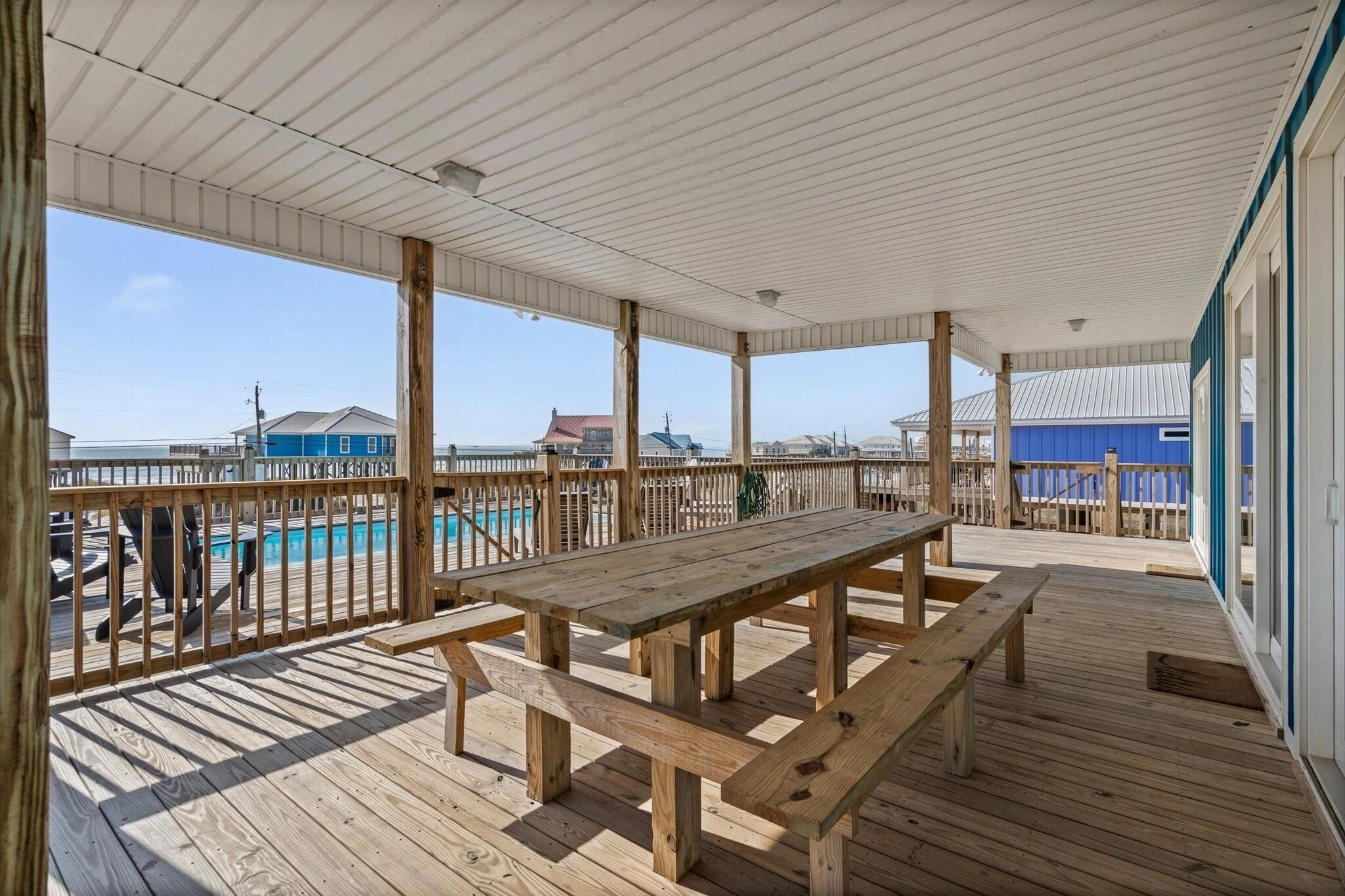 Terraza de madera con mesas de picnic y una piscina al fondo.