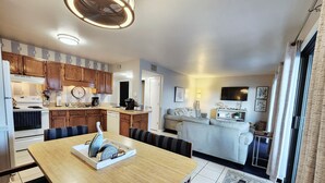 Een moderne keuken met houten kastjes, een eethoek met een houten tafel, en een woonkamer met een bank en een televisie.