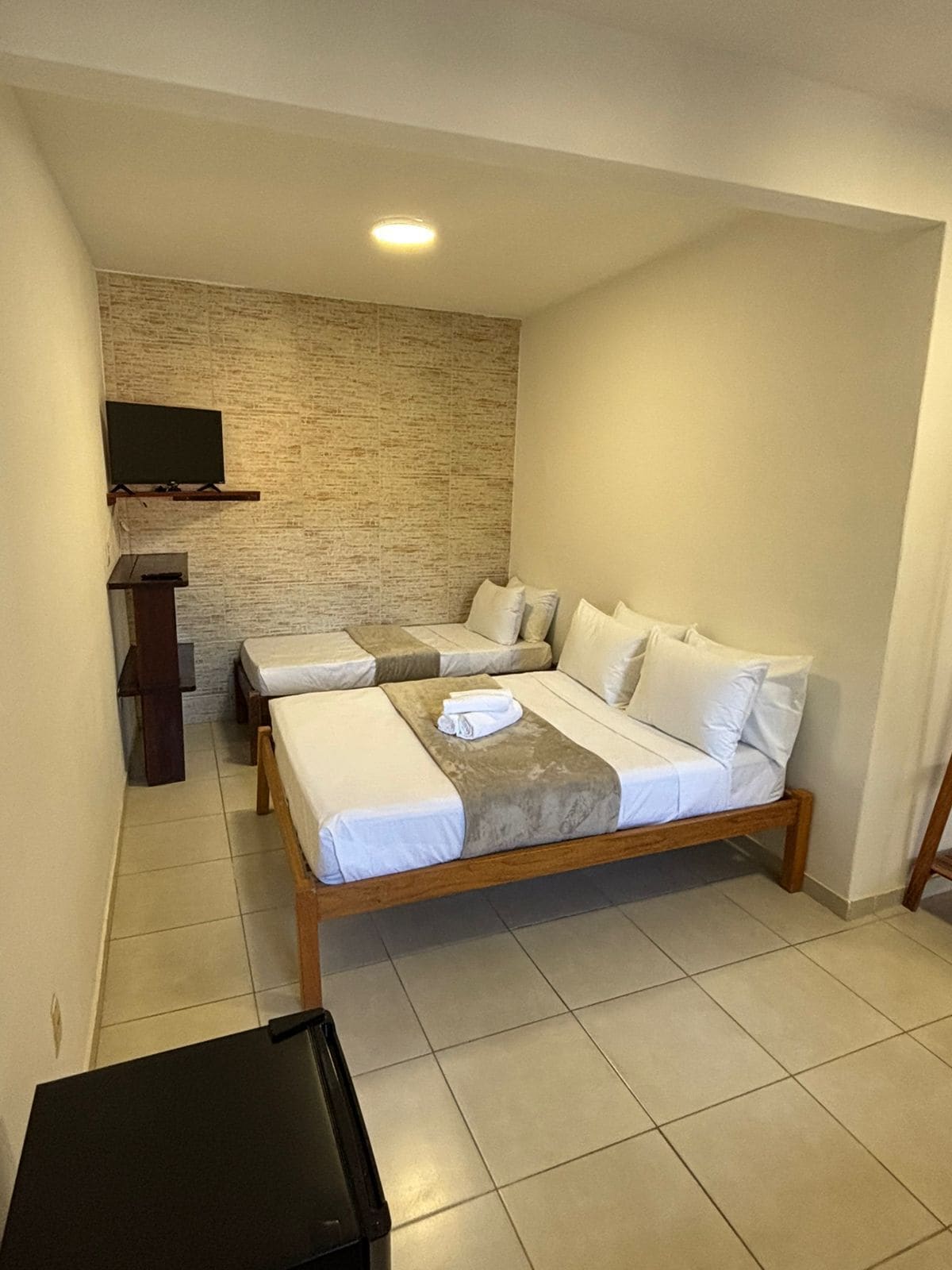 A hotel room with two beds, a flat-screen TV mounted on the wall, and a small table.