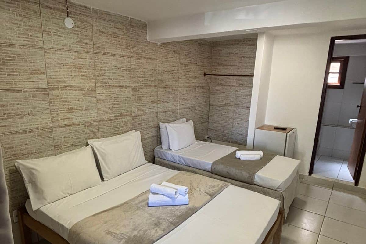 A hotel room with two beds, a wooden headboard, a stone wall, and a tiled floor.