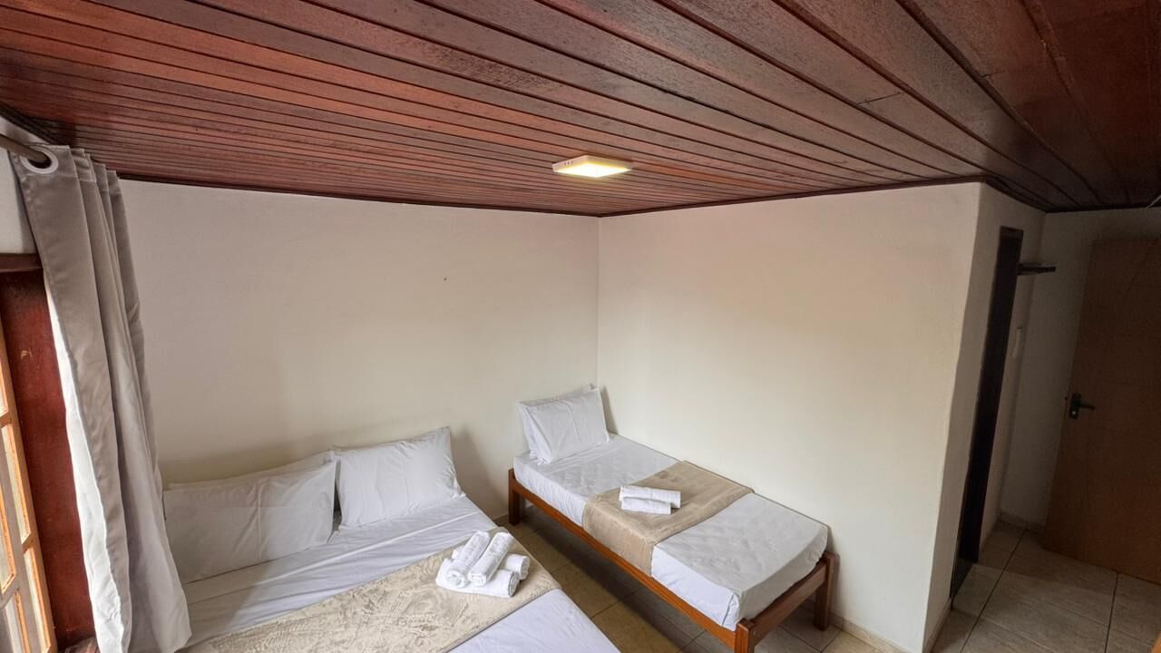 A small, single-room accommodation with two single beds, a wooden ceiling, and a door to the right.
