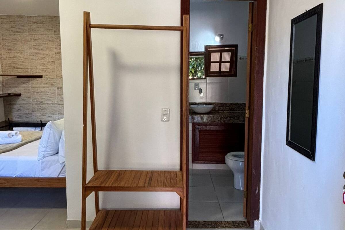 A room with a bed, a wooden bench, a small table, and a bathroom visible through an open door.