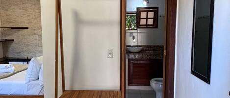 Una habitación con una cama, un banco de madera, una mesita y un baño visible a través de una puerta abierta.