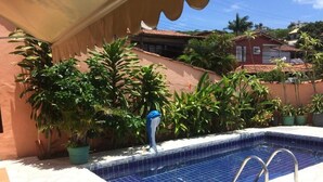 A swimming pool with a tiled edge, surrounded by potted plants and a stone deck. - Go Hotelaria (Búzios)