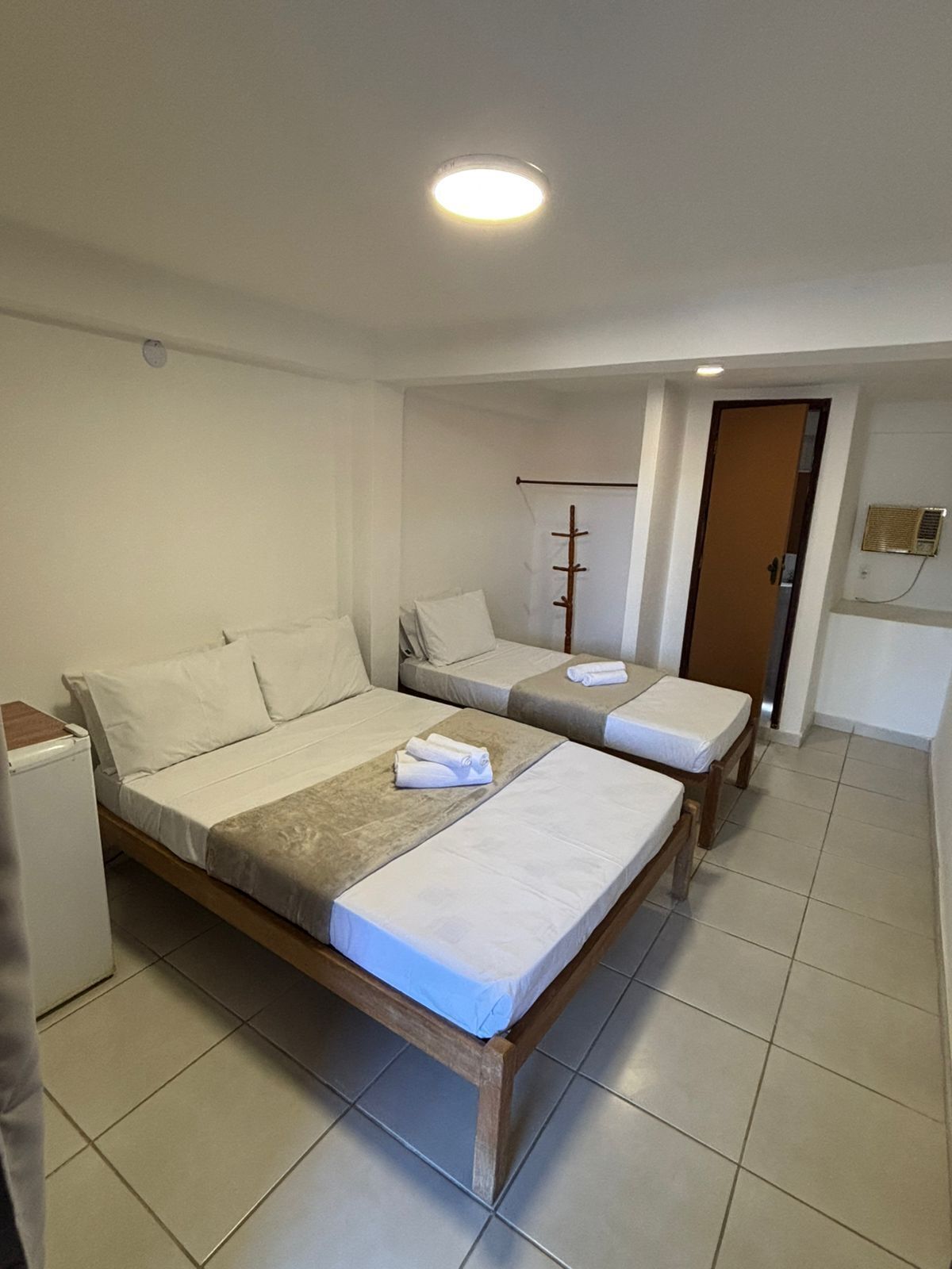Habitación de hotel con dos camas individuales, un pequeño rincón de cocina, una puerta y una luz en el techo.