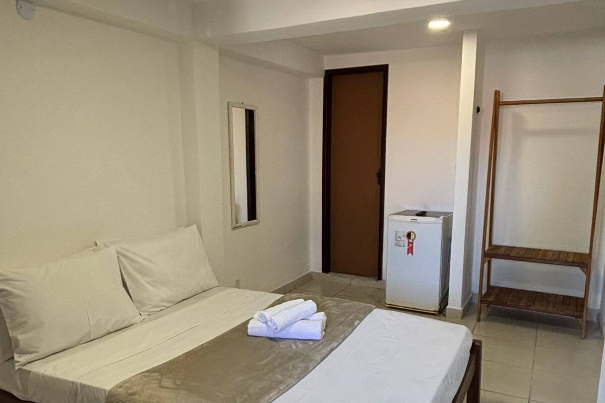 A single-bed room with a wooden frame, a small bedside table, a mirror, a wardrobe, and a ceiling light.