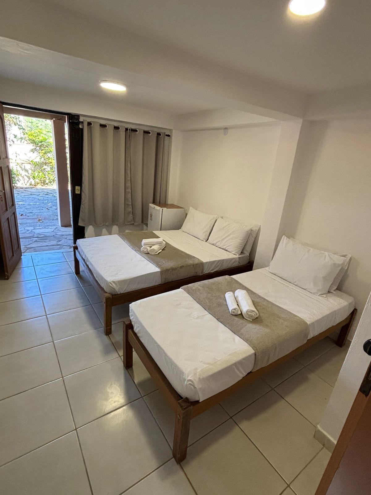 A room with two wooden beds, each with white linens and pillows, a small table, and a window with curtains.