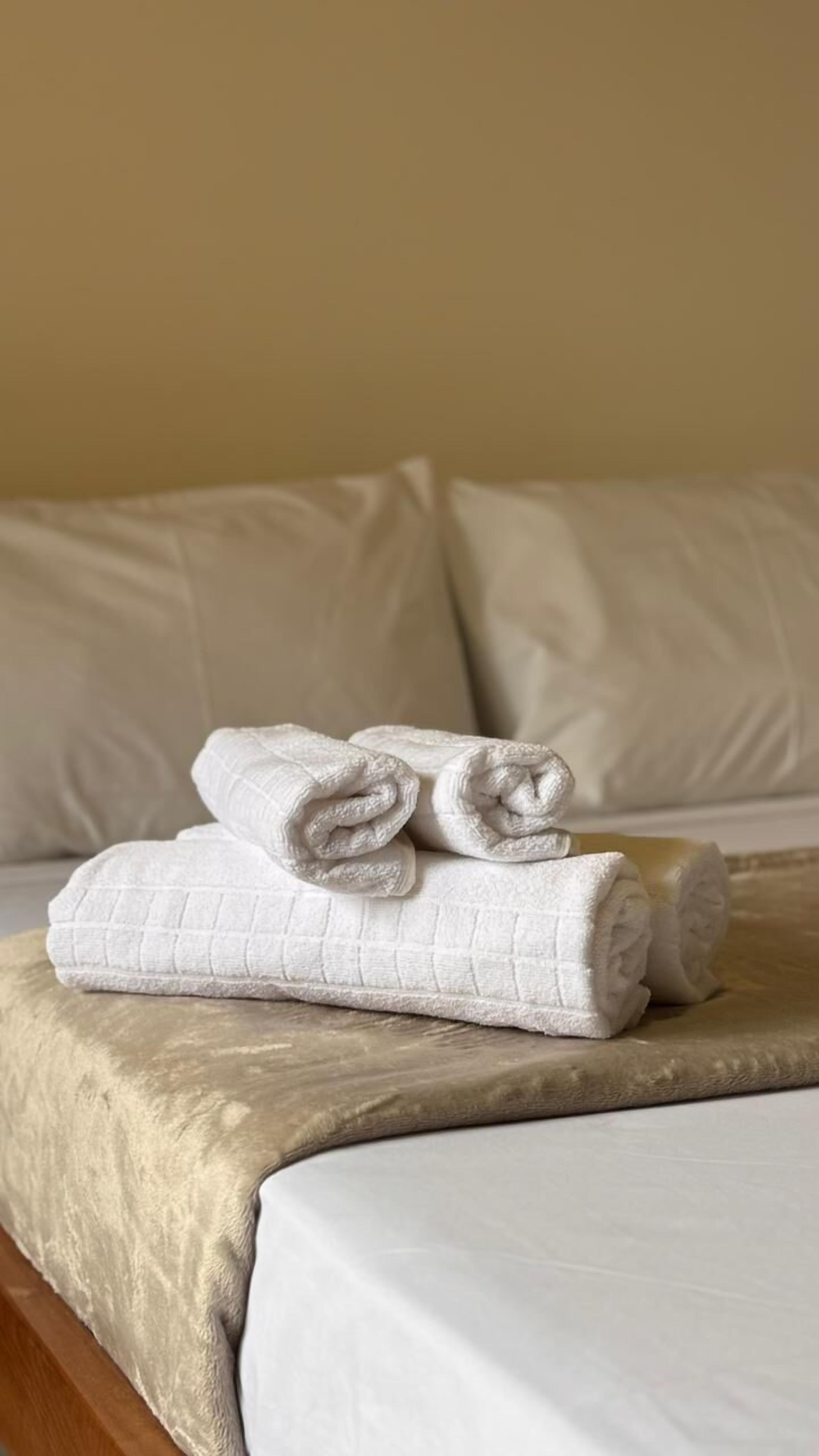 Una cama bien hecha con sábanas blancas y dos toallas enrolladas encima.
