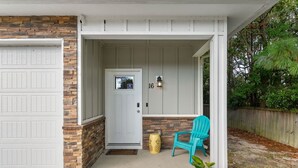 Uma casa com garagem, porta da frente e varanda com uma cadeira.