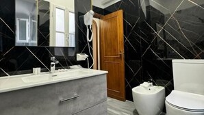 A modern bathroom with a grey vanity, a large mirror, a hairdryer, a toilet, and a bidet.