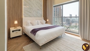 Camera da letto moderna con un letto grande, una parete in marmo, vista sulla città e pavimento in legno.