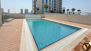 Una piscina sul tetto con un pontile in legno, circondata da grattacieli e palme.