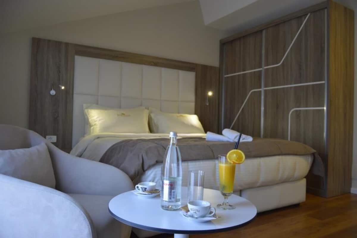 A modern bedroom with a bed, a bedside table with a glass of orange juice, a bottle of water, and a cup.