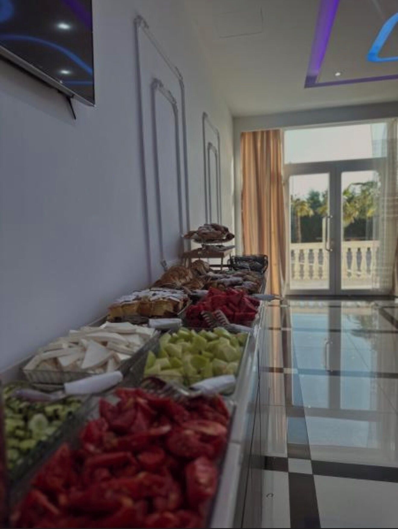 A buffet with various food items, a television mounted on the wall, and a glass door leading outside.