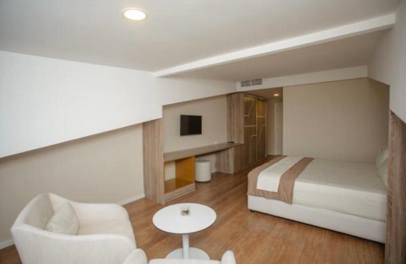 Ein kompaktes Hotelzimmer mit Bett, einer kleinen Sitzecke, einem Fernseher und einer Küchenzeile.