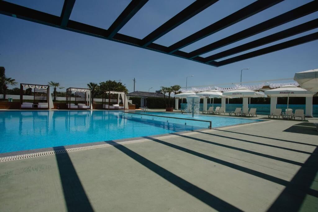 Una piscina con sillas de descanso y sombrillas, rodeada por una zona techada con estructura de techo.